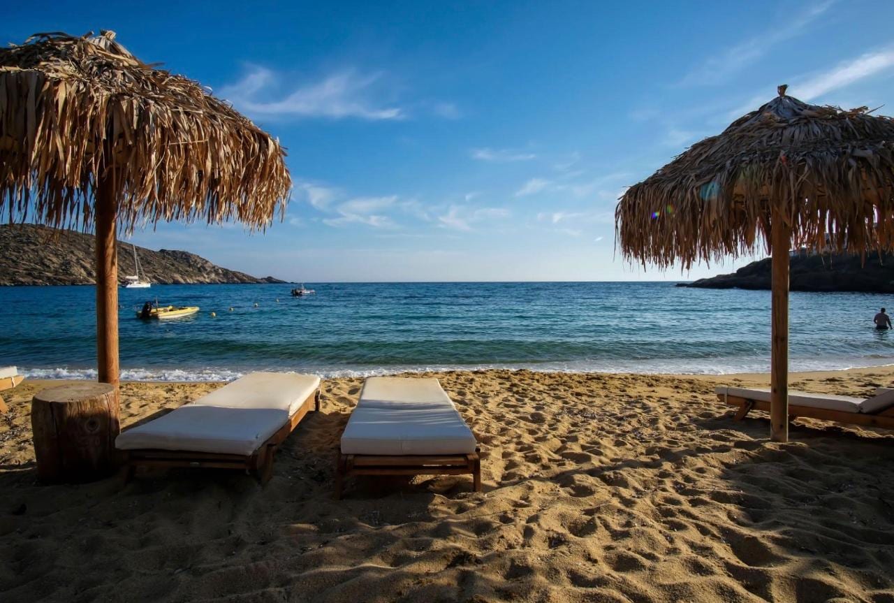 Thatched umbrellas and sunloungers on a golden Ios beach at sundown