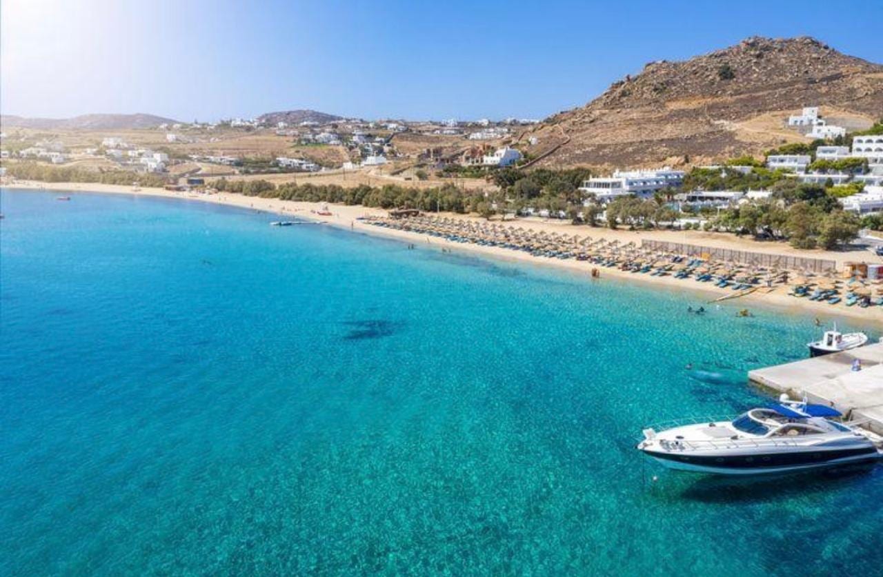 Aerial of a turquoise Mykonos beach with a moored yacht and rows of sunloungers
