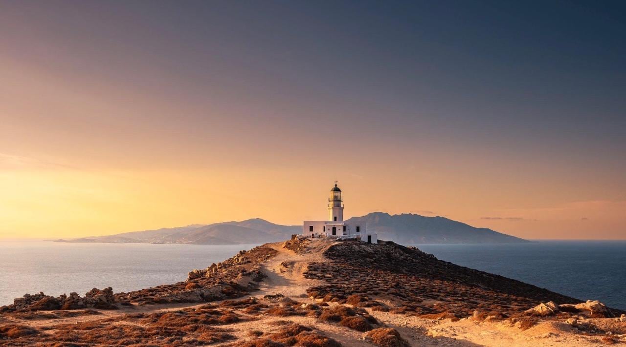 The white Armenistis lighthouse on its headland above a golden Aegean