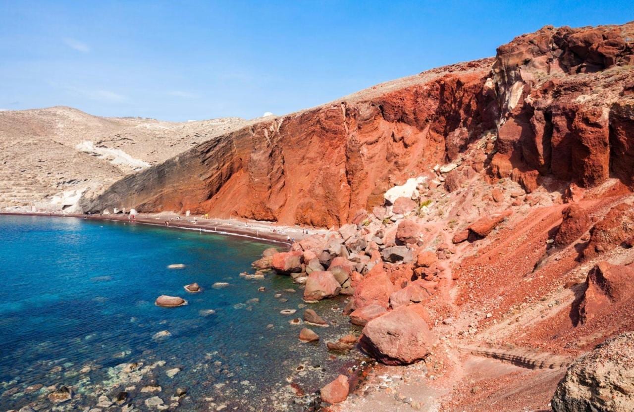 The red volcanic cliffs of Red Beach falling to a turquoise cove