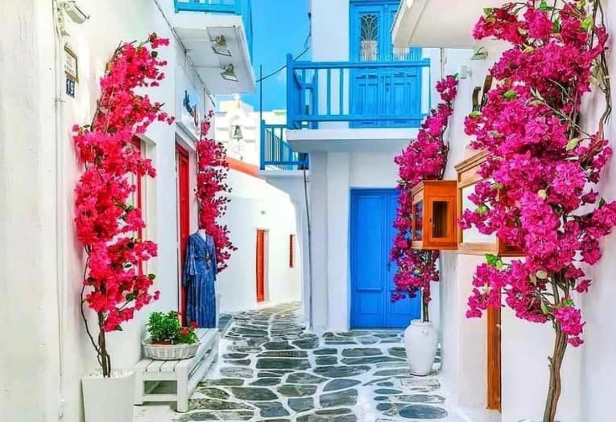 A whitewashed Mykonos lane framed by magenta bougainvillea and a Cycladic-blue door
