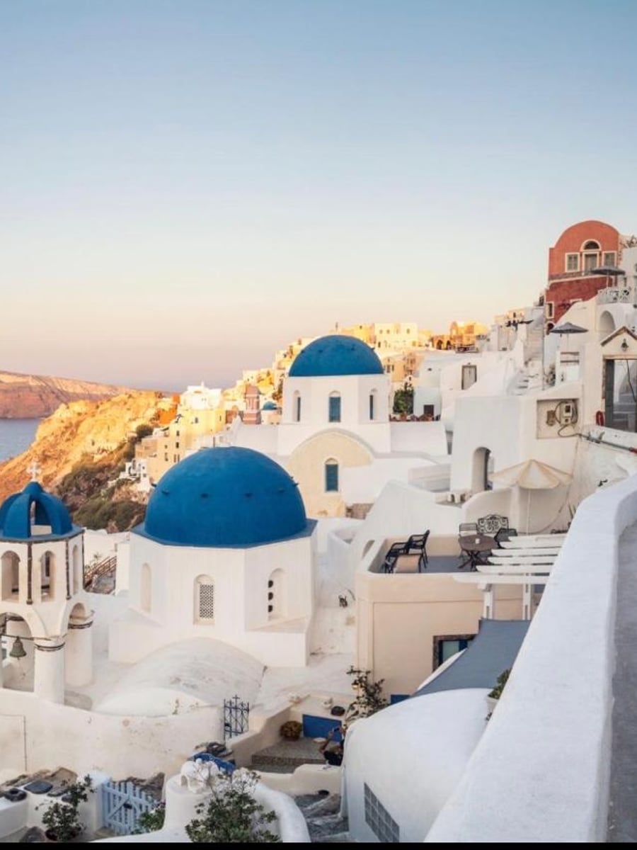 The blue domes and white cave houses of Oia at golden hour above the Santorini caldera
